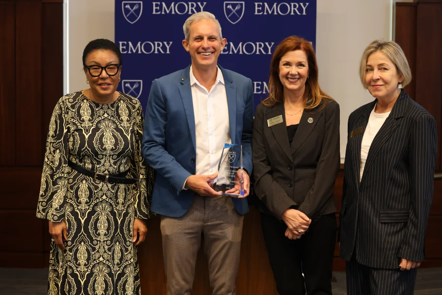 Four attendees pose with the Distinguished Faculty Lecturer award in front of Emory banners